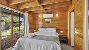 Camera da letto con rivestimento in legno, un letto, lampade sui comodini e una finestra con vista sul verde.