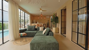 A modern living room with a sectional sofa, a ceiling fan, pendant lights, and a view of a pool. - Ksamil Villa with Private Pool & Jacuzzi – Serein (Ksamil)