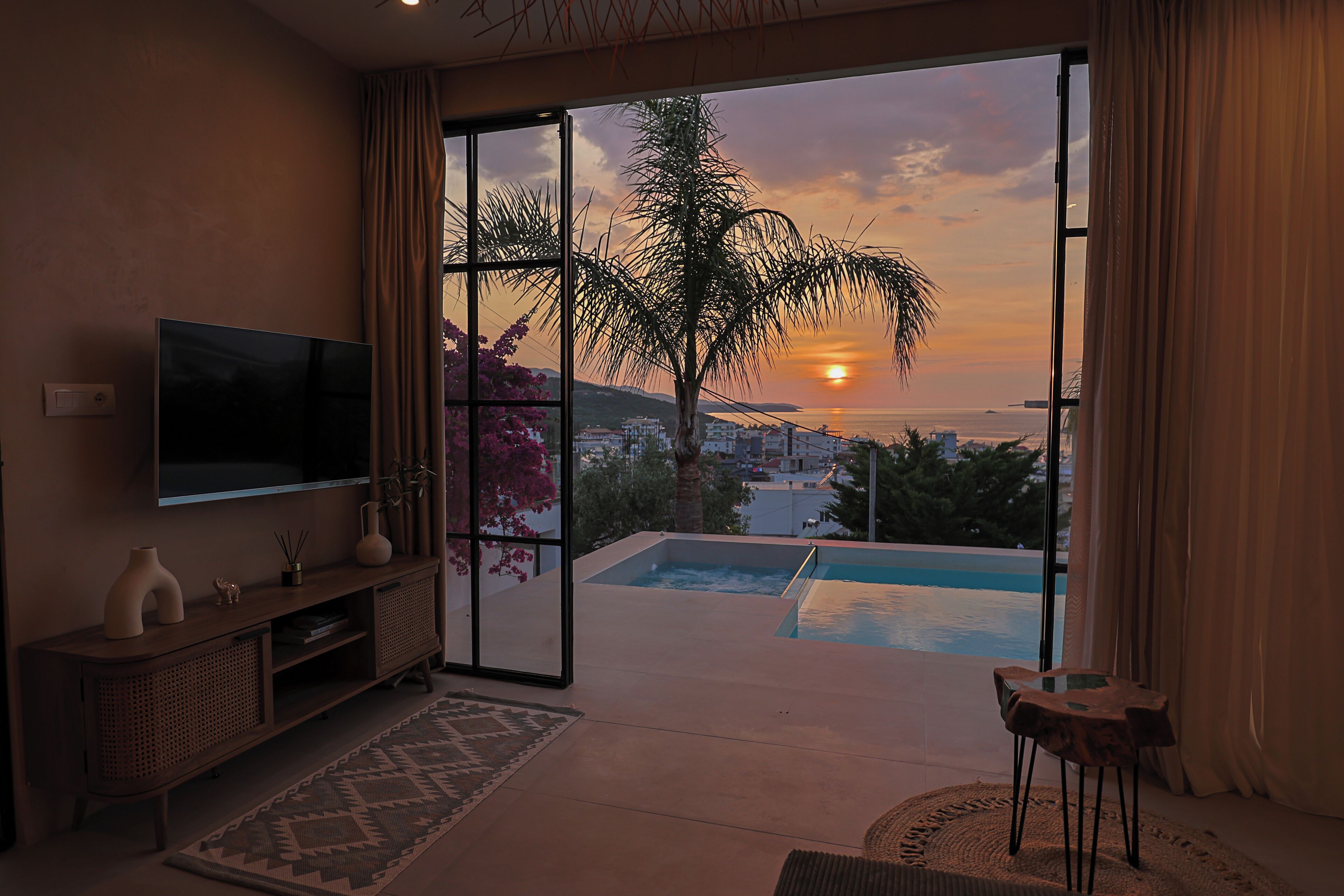 A room with a TV, a pool, and a view of the sunset.