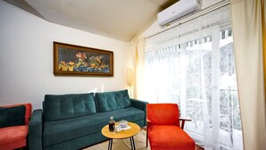 Un salon avec un canapé vert, un fauteuil rouge, une petite table basse en bois et un tableau accroché au mur.