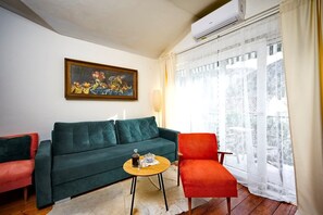 Ein Wohnzimmer mit einem grünen Sofa, einem roten Sessel, einem kleinen Holztisch und einem Bild an der Wand.