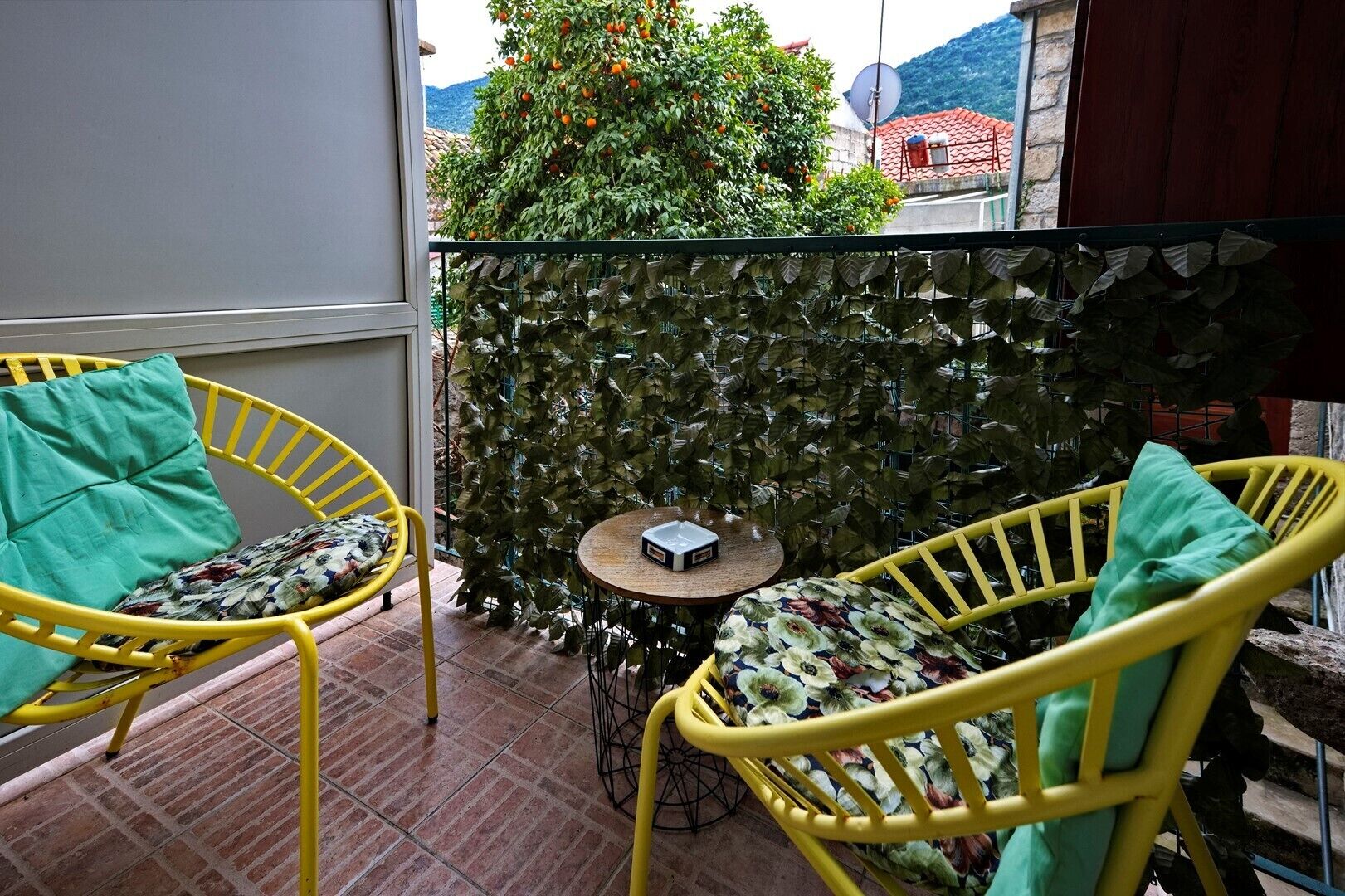 Ein Balkon mit gelben Stühlen, einem Tisch und einer grünen, blattbewachsenen Wand.