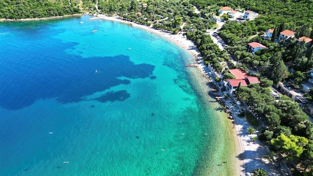 An aerial view of a coastal area with clear turquoise waters, a sandy beach, and a row of houses with red roofs. - One-Bedroom Apartment Senko A2 (Trpanj)