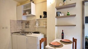 Una cocina compacta con un lavabo, una cafetera y un refrigerador pequeño. Hay una mesa de comedor con algunos platos y una botella de vino.