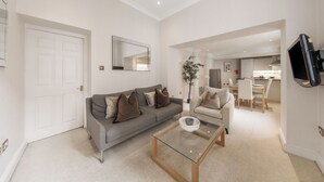 A living room with a sofa, armchair, coffee table, and a dining area with a table and chairs. - Hertford Flat 5 (London)