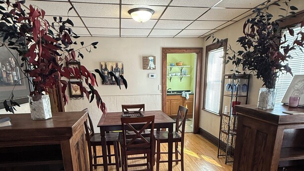 Uma sala de jantar com uma mesa e cadeiras de madeira, teto com iluminação embutida e uma porta de entrada para uma cozinha.