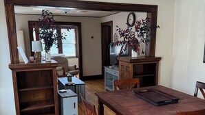 Uma sala de jantar com uma mesa de madeira, cadeiras, uma TV e uma planta.