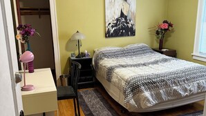Quarto com cama, escrivaninha, cadeira e um quadro na parede.