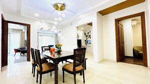 A spacious dining area with a high ceiling, a modern chandelier, and a view into the adjacent room. - Bout Hotel and Banquet Hall Gurgaon (Gurugram)