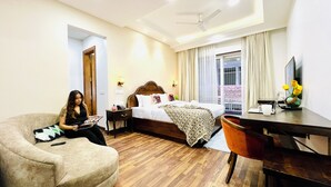 A hotel room with a bed, a desk, a chair, a television, and a window with curtains. - Bout Hotel and Banquet Hall Gurgaon (Gurugram)