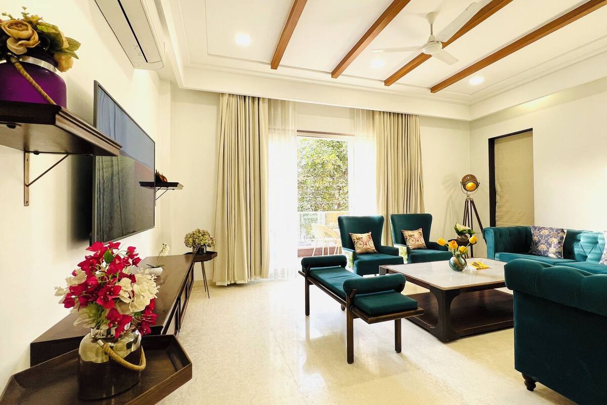 A modern living room with a TV, two green sofas, a coffee table, and a floor lamp.