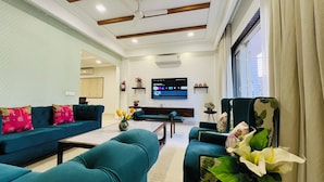 A spacious living room with teal sofas, a coffee table, and a TV mounted on the wall. - Bout Hotel and Banquet Hall Gurgaon (Gurugram)