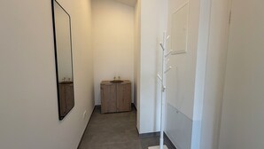 Un pasillo estrecho con un armario de madera, un perchero blanco y un espejo en la pared.