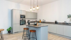 A modern kitchen with a central island, bar stools, a built-in oven, and pendant lighting. - Morningside Private Residence (Edinburgh)
