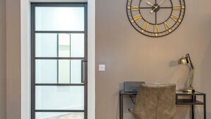 A room with a large wall clock, a desk with a laptop, a chair, and a door leading to a balcony. - Morningside Private Residence (Edinburgh)