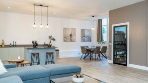 A modern living room with a blue sofa, a glass coffee table, and a dining area with a table and chairs. - Morningside Private Residence (Edinburgh)