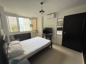 A bedroom with a bed, a desk, a chair, a fan, a TV, and a door. - El Laguito Beach Cartagena (Cartagena)
