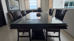 Un comedor con mesa de vidrio, sillas negras, ventilador de techo y un ventanal con vistas.