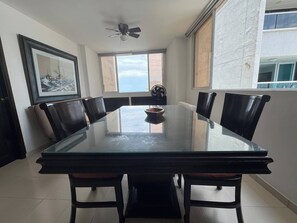 A dining area with a glass table, black chairs, a ceiling fan, and a large window with a view. - El Laguito Beach Cartagena (Cartagena)