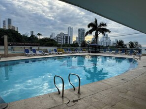 A swimming pool with lounge chairs, a palm tree, and a cityscape in the background. - El Laguito Beach Cartagena (Cartagena)