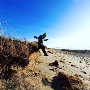 Une personne court sur une plage de sable, avec de l’herbe sur le côté gauche.