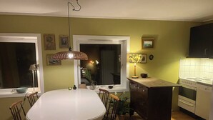 Uma sala de jantar com uma mesa e cadeiras brancas, uma cozinha com eletrodomésticos brancos e uma janela com vista.