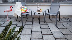 Eine Terrasse mit zwei Stühlen, einem Tisch mit Vase und Früchten sowie einer Flamingo-Statue.