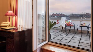 Ein Hotelzimmer mit Schreibtisch, Stuhl, Tisch, Lampe und Blick auf einen Balkon mit Stuhl und Tisch.