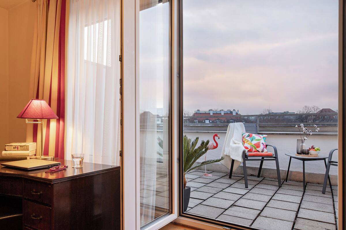 Habitación de hotel con escritorio, una silla, una mesa, una lámpara y vistas a un balcón con una silla y una mesa.