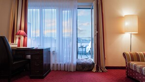 Ein Hotelzimmer mit Schreibtisch, Stuhl, Sofa und Blick auf die Stadt durch ein großes Fenster.