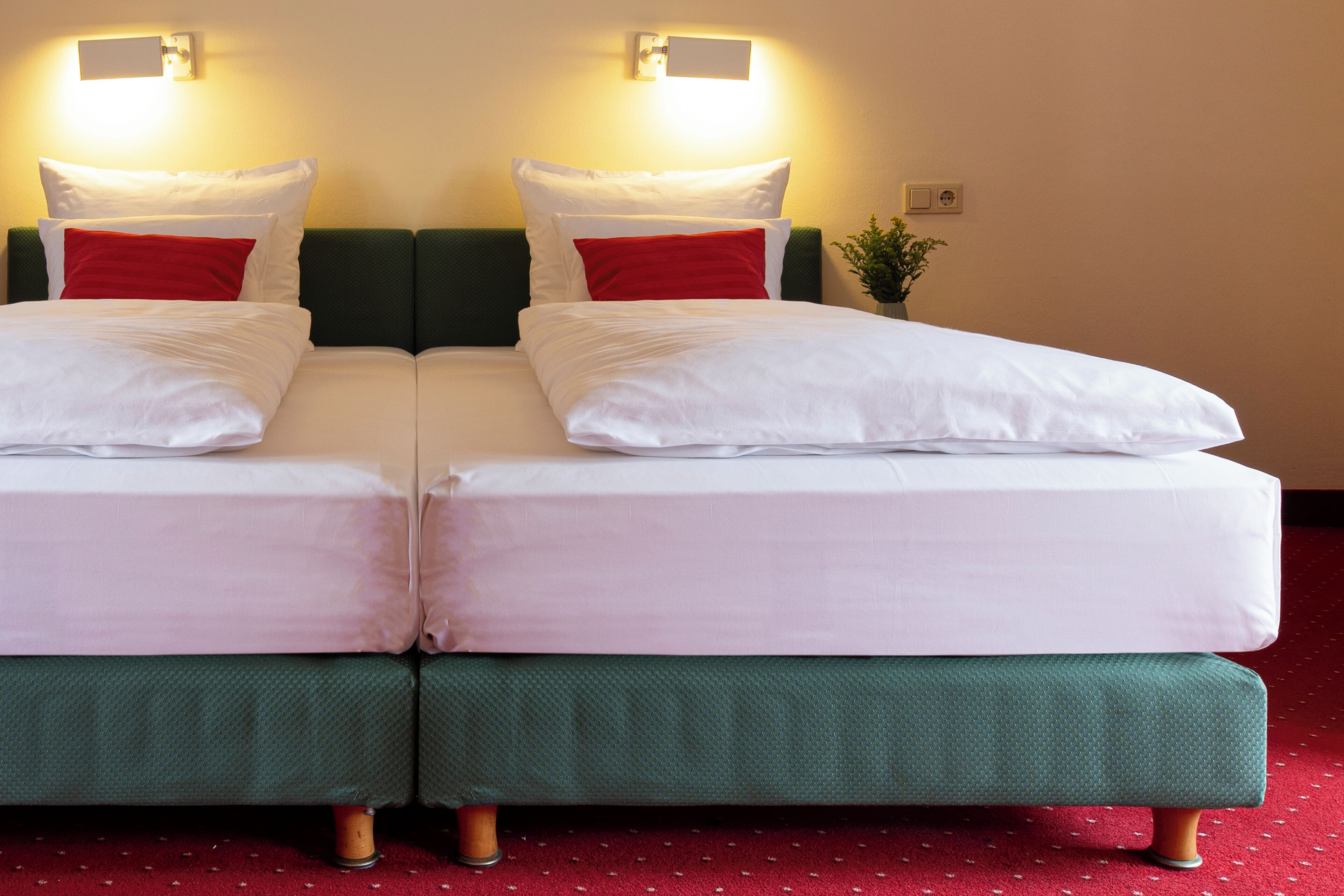 A double bed with white and red bedding, green headboards, and a red carpet.