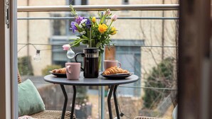 Un balcó amb una taula preparada per esmorzar, incloent croissants, tasses de cafè i un ram de flors.