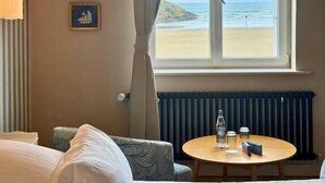 Ein Hotelzimmer mit einem Bett, einem runden Tisch mit Flasche und Gläsern, einem Stuhl, Blick auf den Strand und einem Heizkörper.