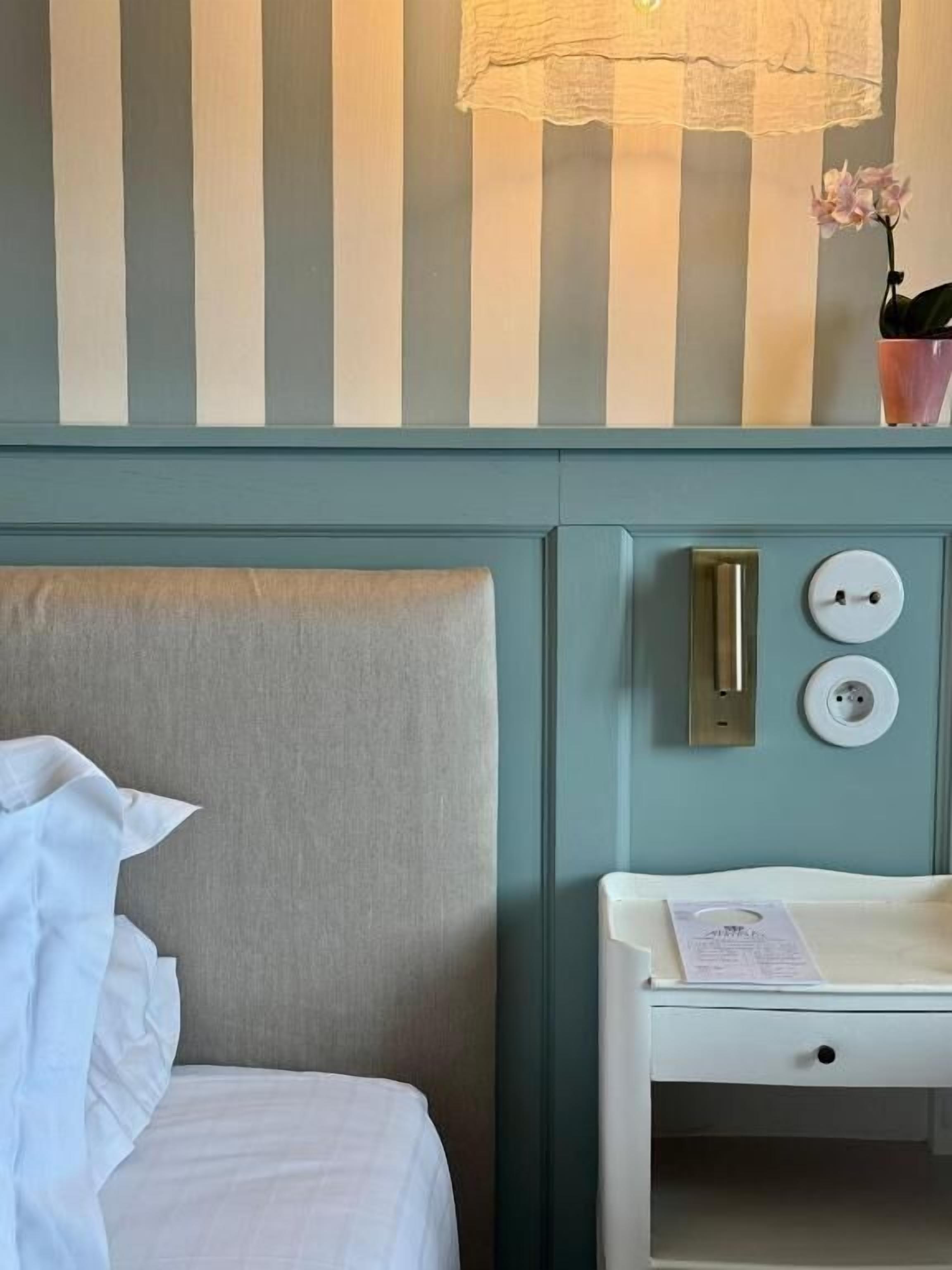 Une chambre d’hôtel avec un lit, une table de chevet avec une lampe et une prise de courant fixée au mur.