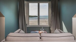 Ein Hotelzimmer mit großem Fenster, zwei Betten, einem kleinen Tisch mit Flasche und Gläsern sowie Vorhängen.
