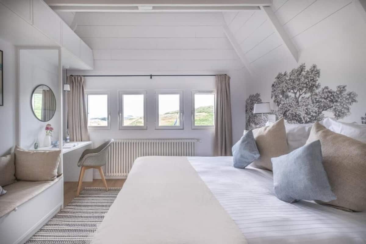 A bedroom with a bed, a desk, a chair, and a view of the outdoors.