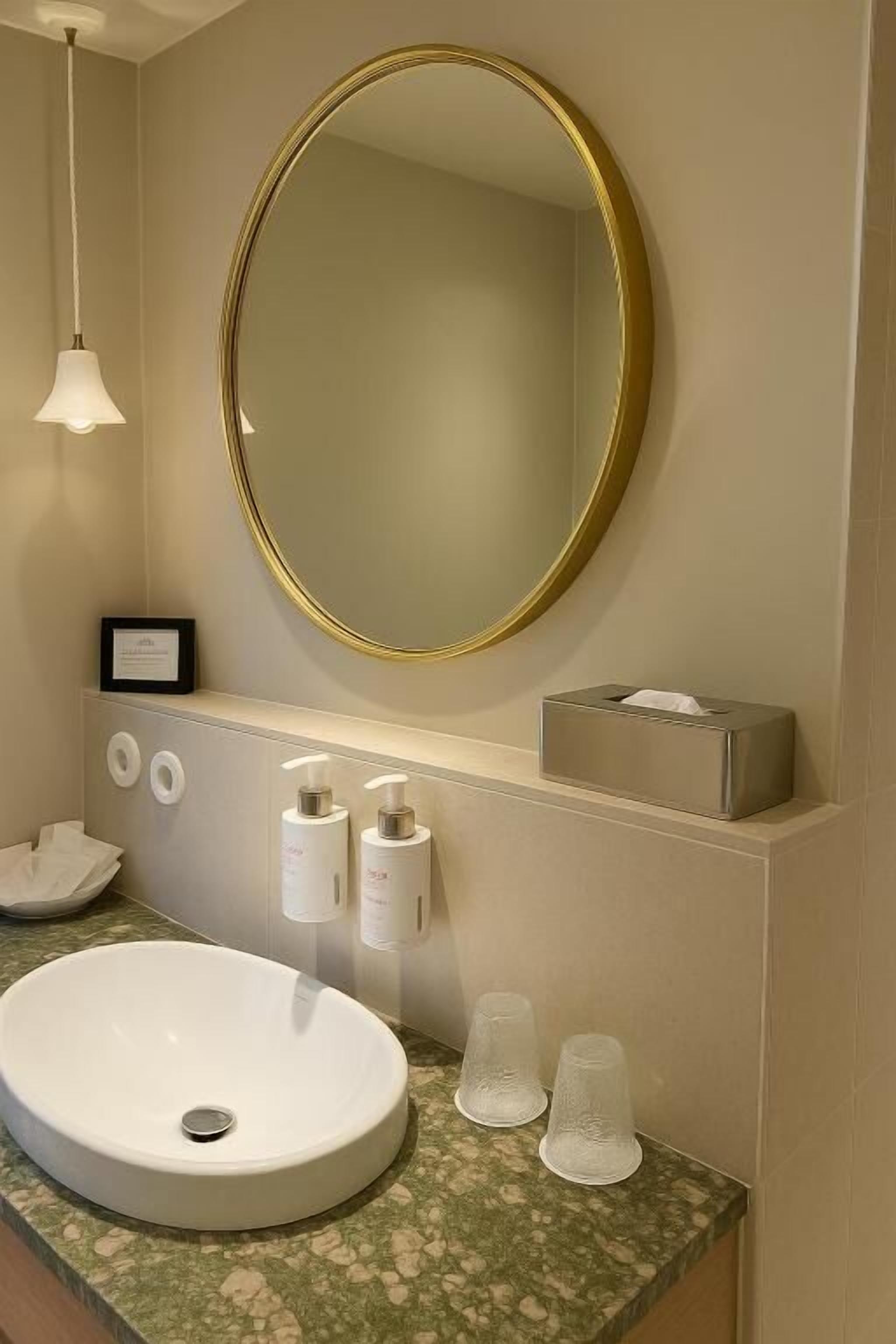 A bathroom with a round mirror, a white sink, and a marble countertop.