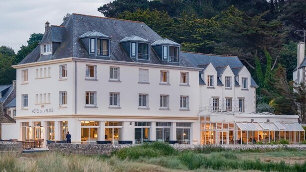 Ein großes, mehrstöckiges Hotel mit weißer Fassade, zahlreichen Fenstern und einem Restaurantbereich mit Außenplätzen.