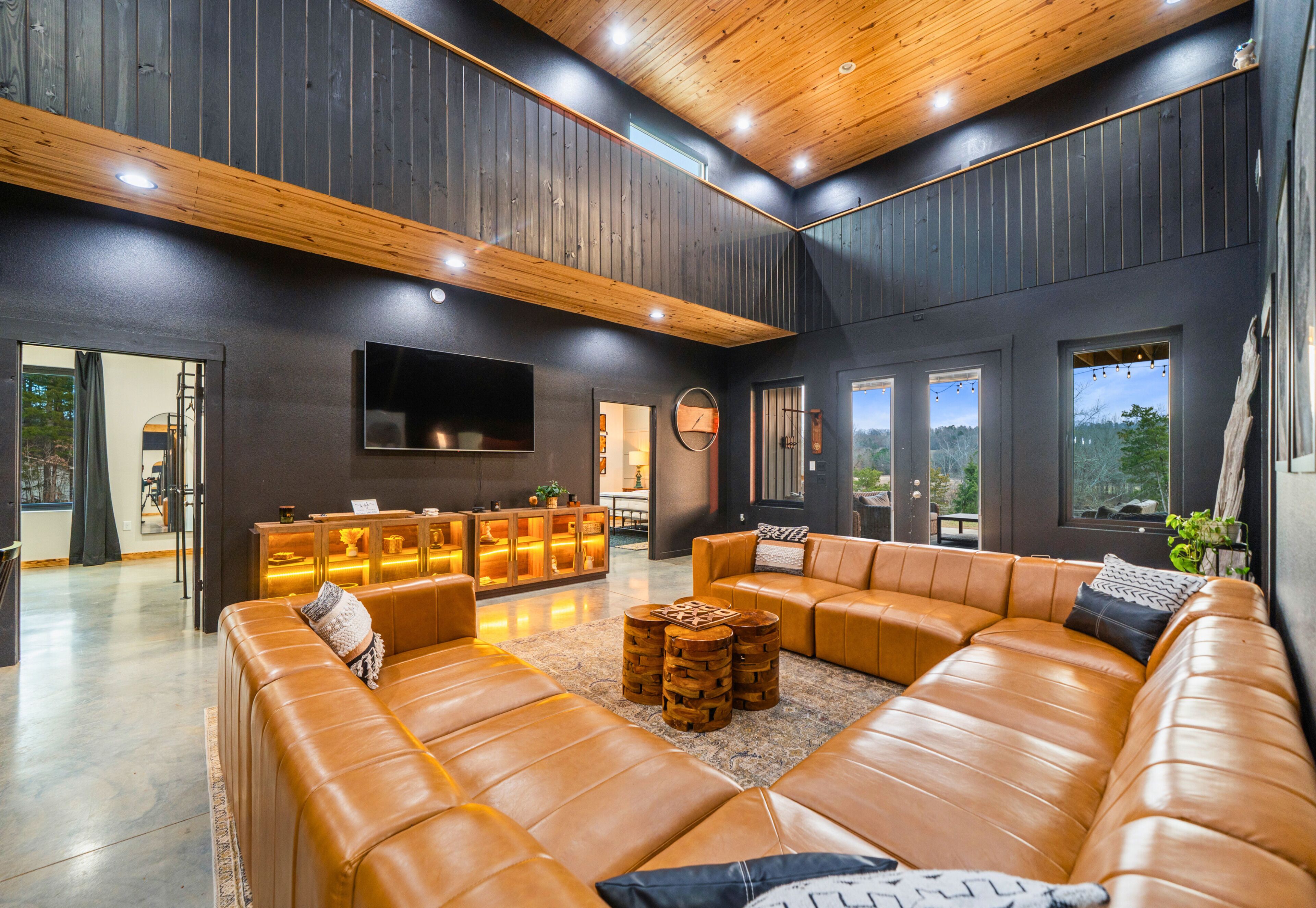 A spacious living area with a large leather sofa, wooden accents, and a flat-screen TV mounted on the wall.