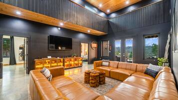A spacious living area with a large leather sofa, wooden accents, and a flat-screen TV mounted on the wall.