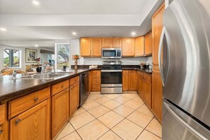 A modern kitchen with wooden cabinets, stainless steel appliances, and a tiled floor. - SUMMER SALE! 3BR Townhouse with Ocean Views Near Beach & Pool - KPL 15 (Lahaina)