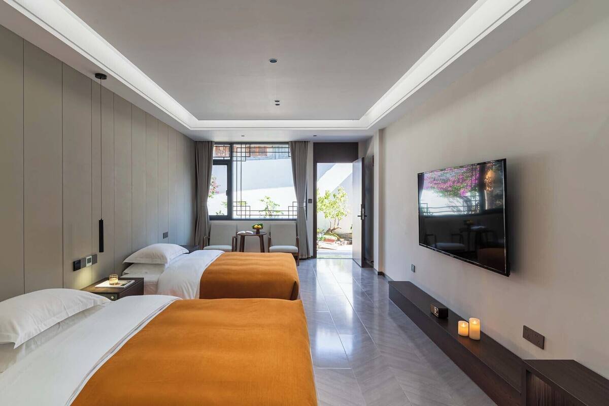 Habitación de hotel con dos camas, televisión, una mesita y vista al exterior.