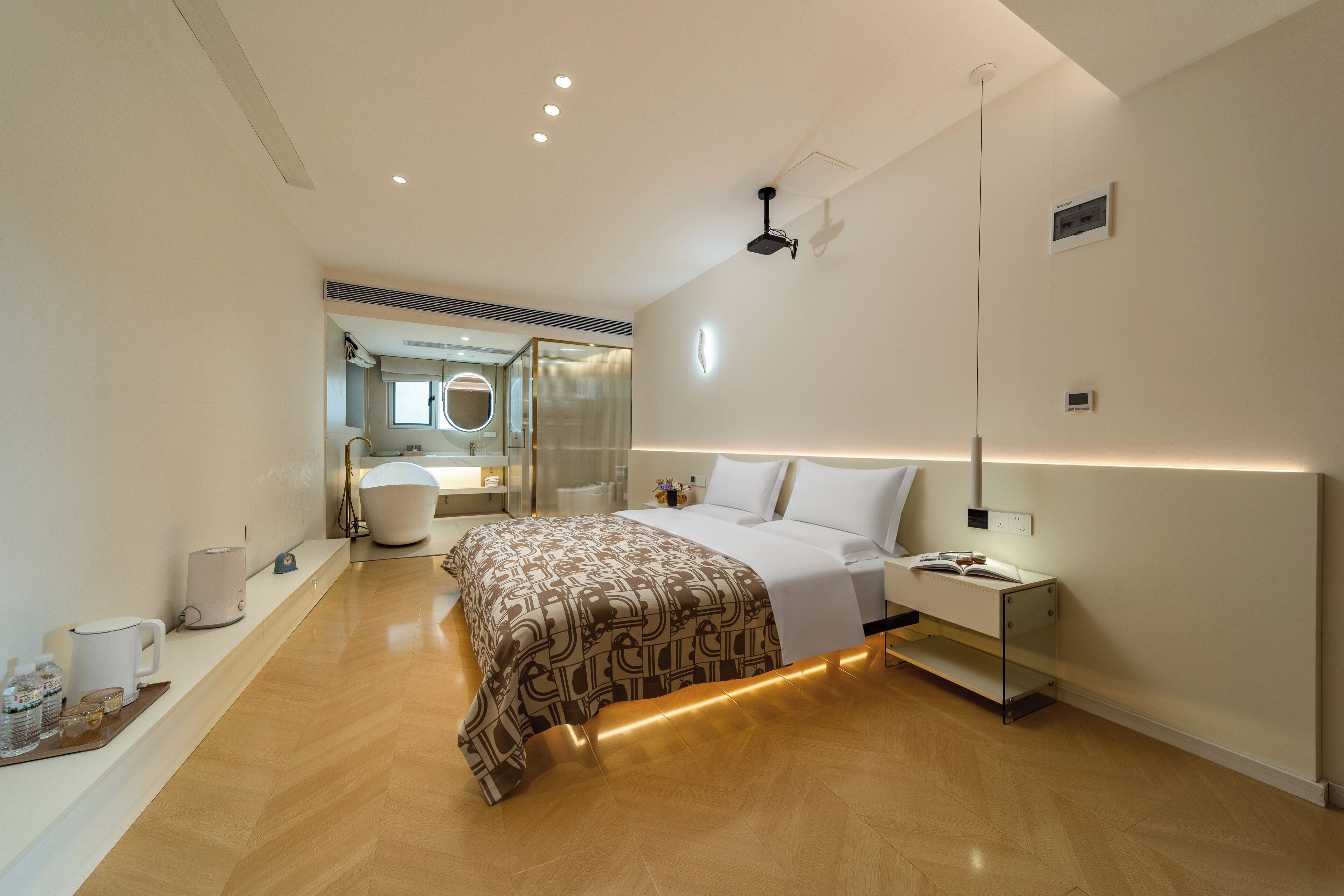 Un dormitorio moderno con cama, mesitas de noche, un espejo y un baño visible al fondo.