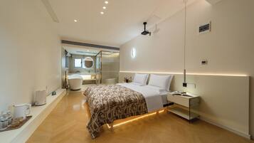 Un dormitorio moderno con cama, mesitas de noche, un espejo y un baño visible al fondo.