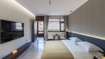 A modern hotel room with a large bed, a flat-screen TV, a small table with chairs, and a view of traditional architecture outside the window.
