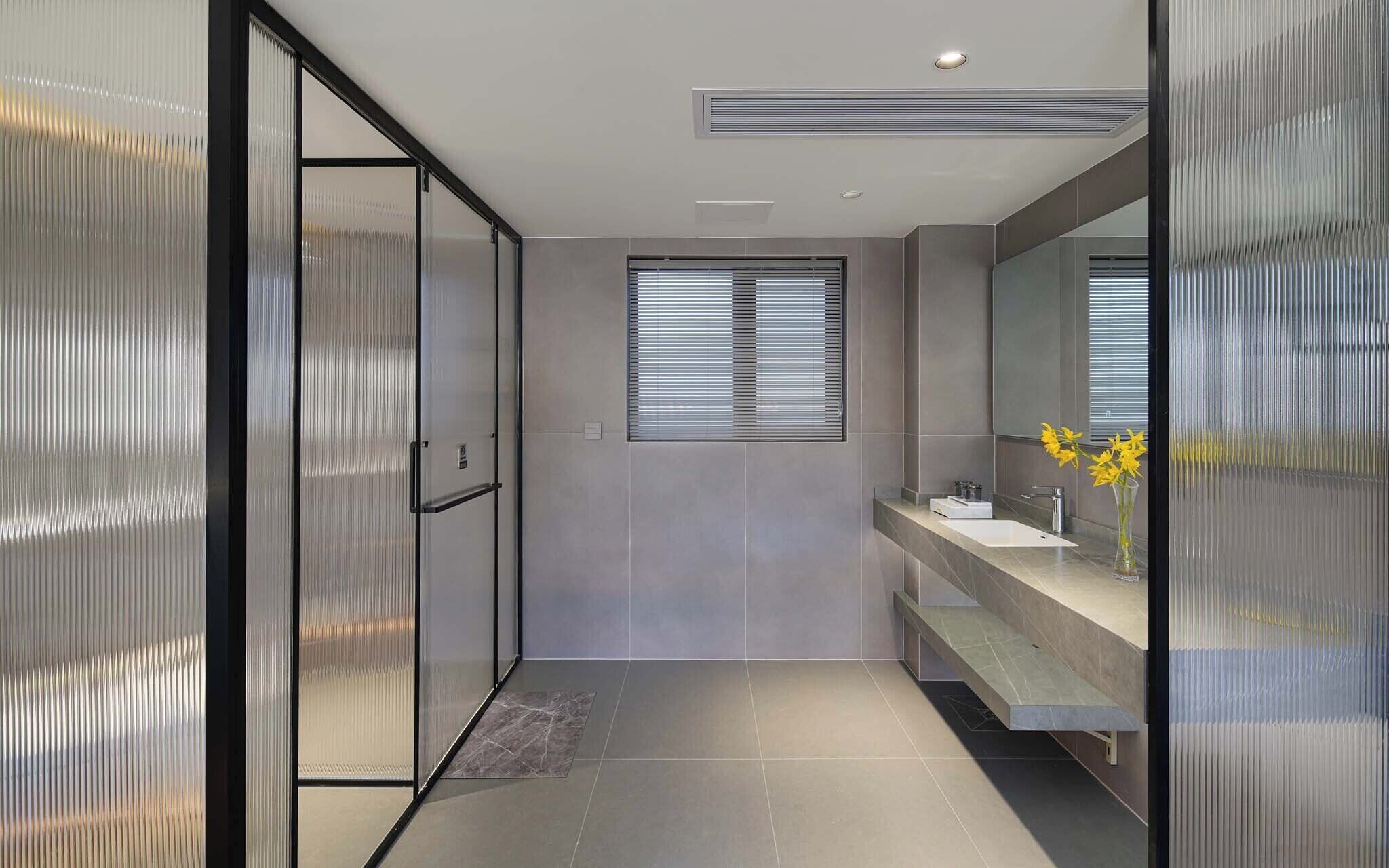 A modern bathroom with a glass shower enclosure, a window with blinds, and a vanity with a mirror.