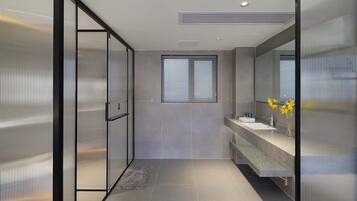 A modern bathroom with a glass shower enclosure, a window with blinds, and a vanity with a mirror.