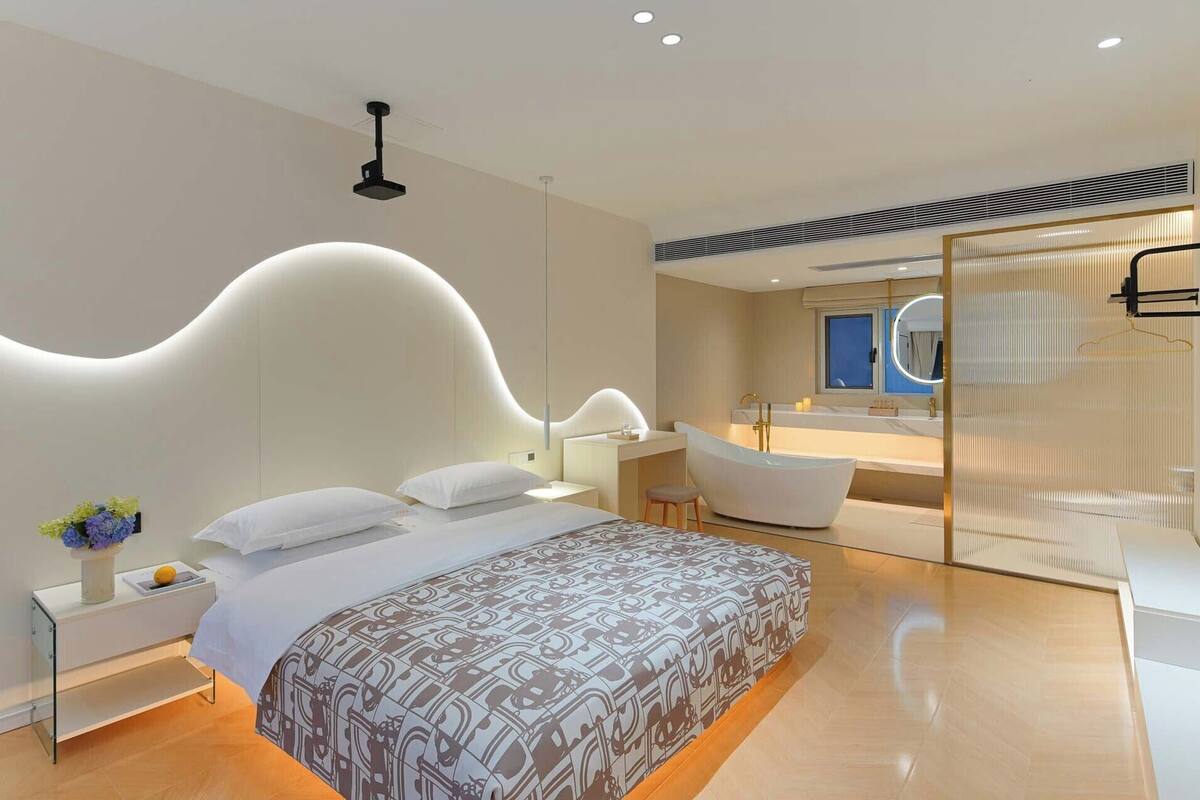 Un dormitorio moderno con cabecera curva, cama grande, zona de estar, bañera y baño con espejo grande.