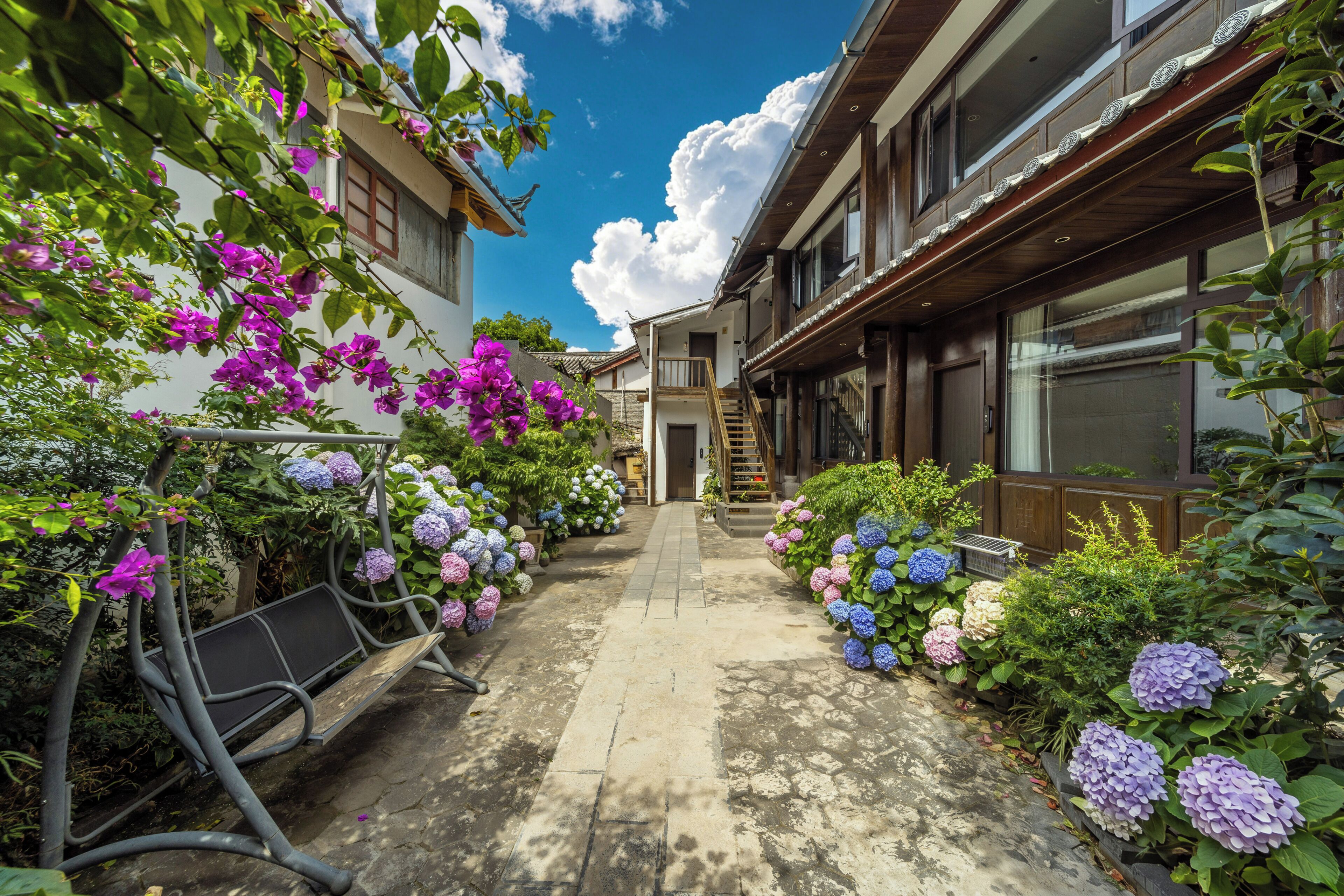 A courtyard with a pathway flanked by vibrant flowers and a building with traditional architecture.