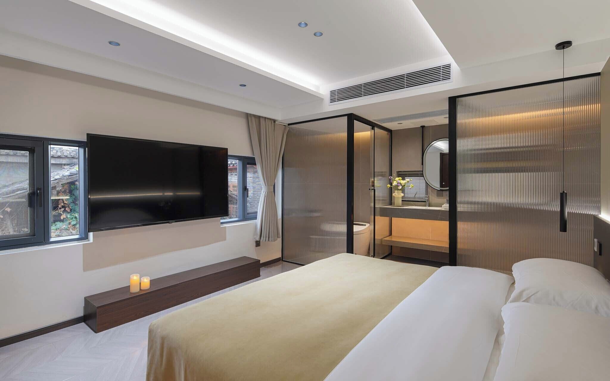 Een moderne hotelkamer met een groot bed, een flatscreen televisie, een badkamer met spiegel en een raam met gordijnen.